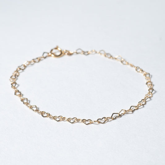 Dainty gold heart shaped chain bracelet on white background. 