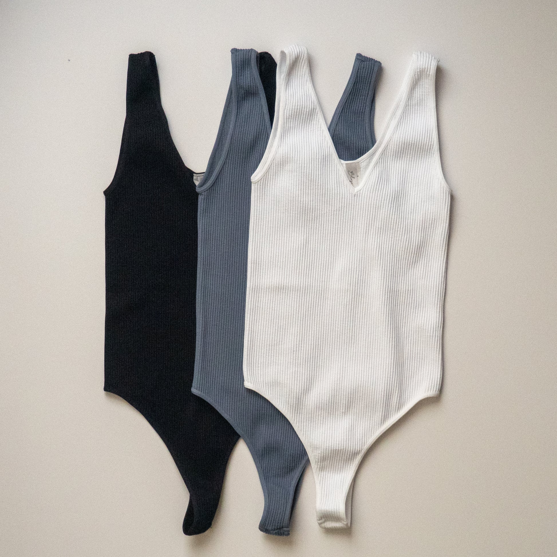 Ribbed V-neck seamless thong bodysuits. Black, Bluestone, and White